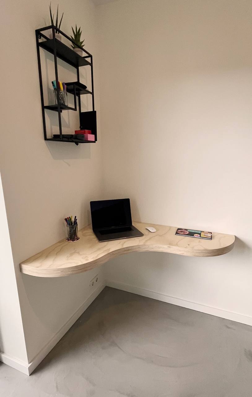 Zwevend gebogen multiplex bureau in een hoek met wandplank