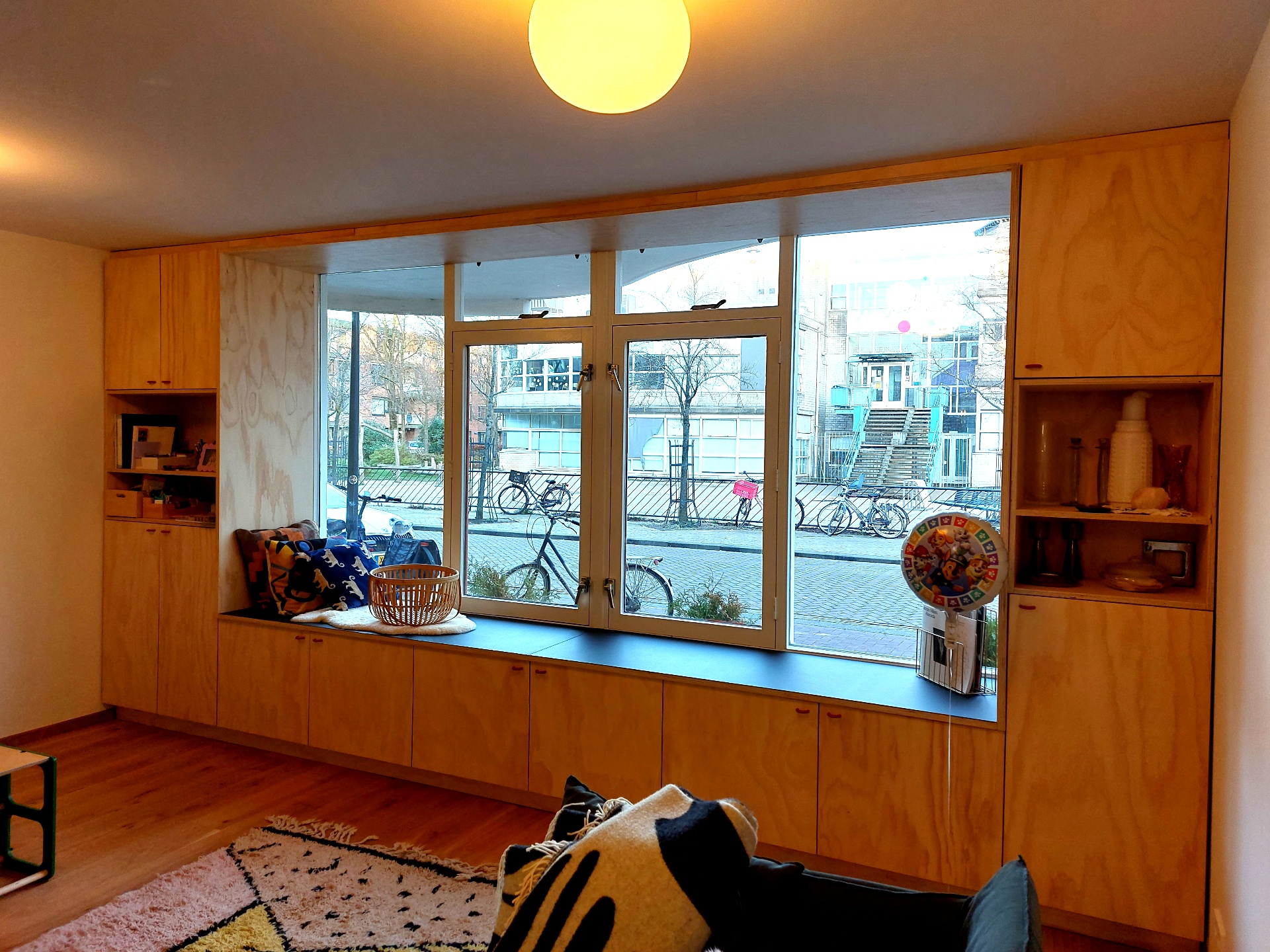 Wandvullend multiplex meubel rond het raam met zitbank en opbergkasten