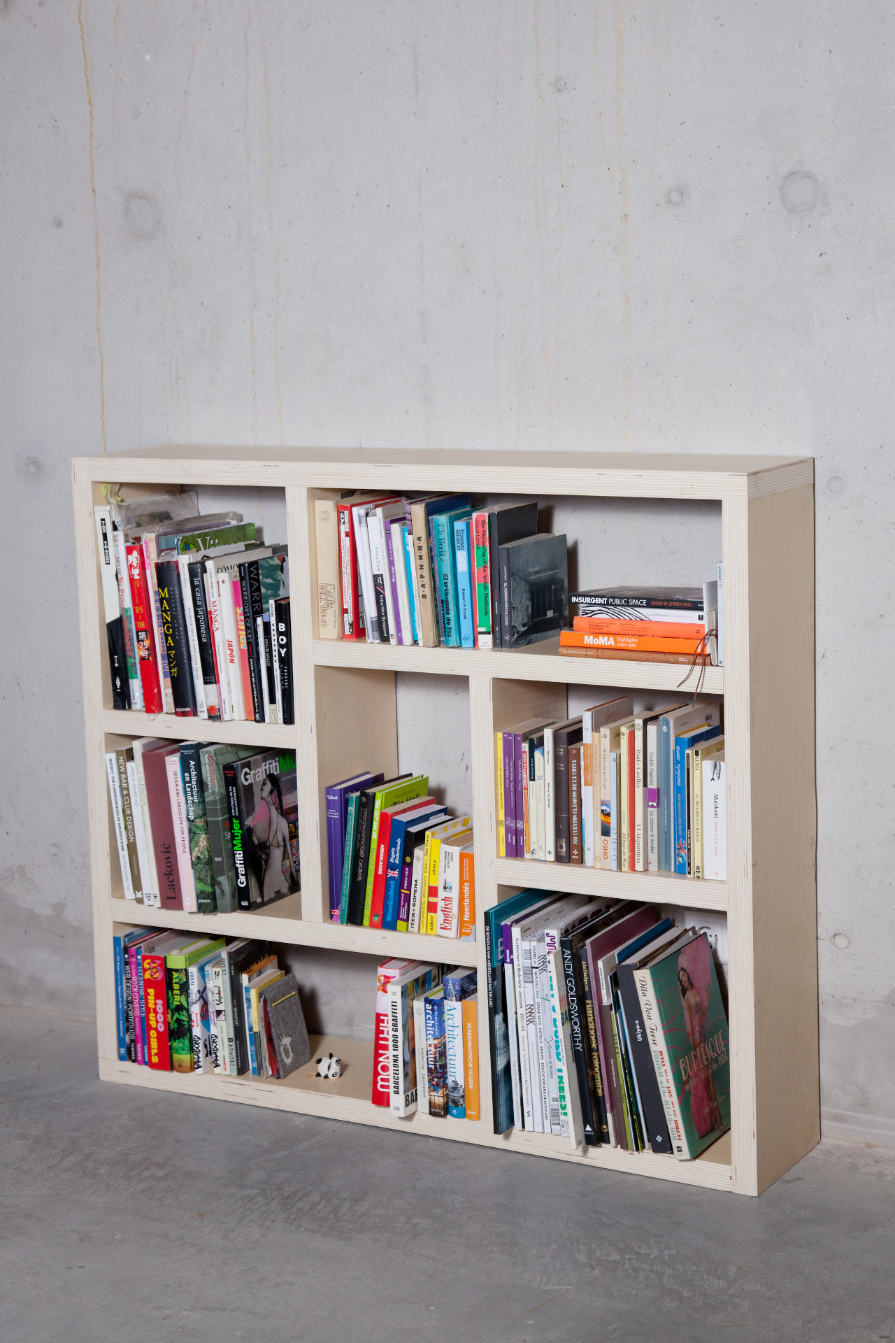 Lage open boekenkast in licht hout tegen een betonnen wand