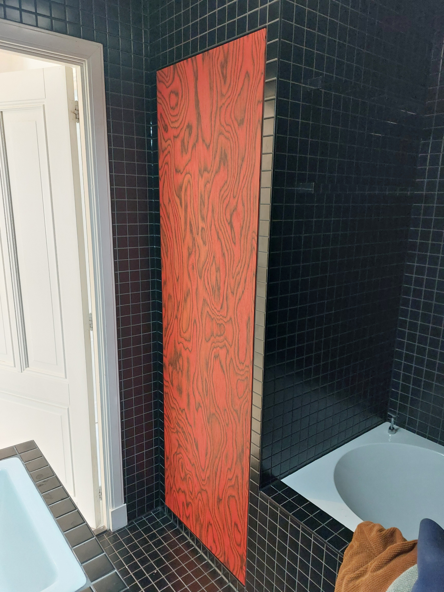 Rood gebeitst houtnerf paneel in zwart betegelde badkamer